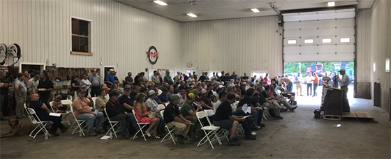 A speaker in front of a crowd of sitting attendees in a warehouse.