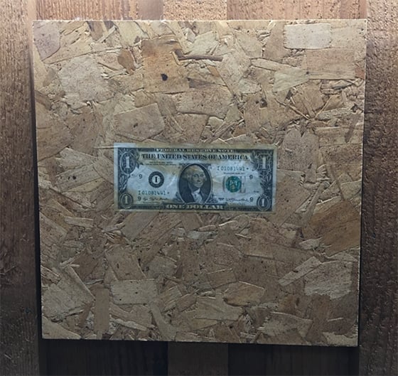 A one dollar bill pasted to a piece of OSB.