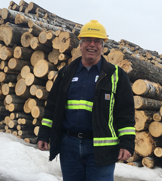 a photo of Jerry Richards in front of a pile of timber